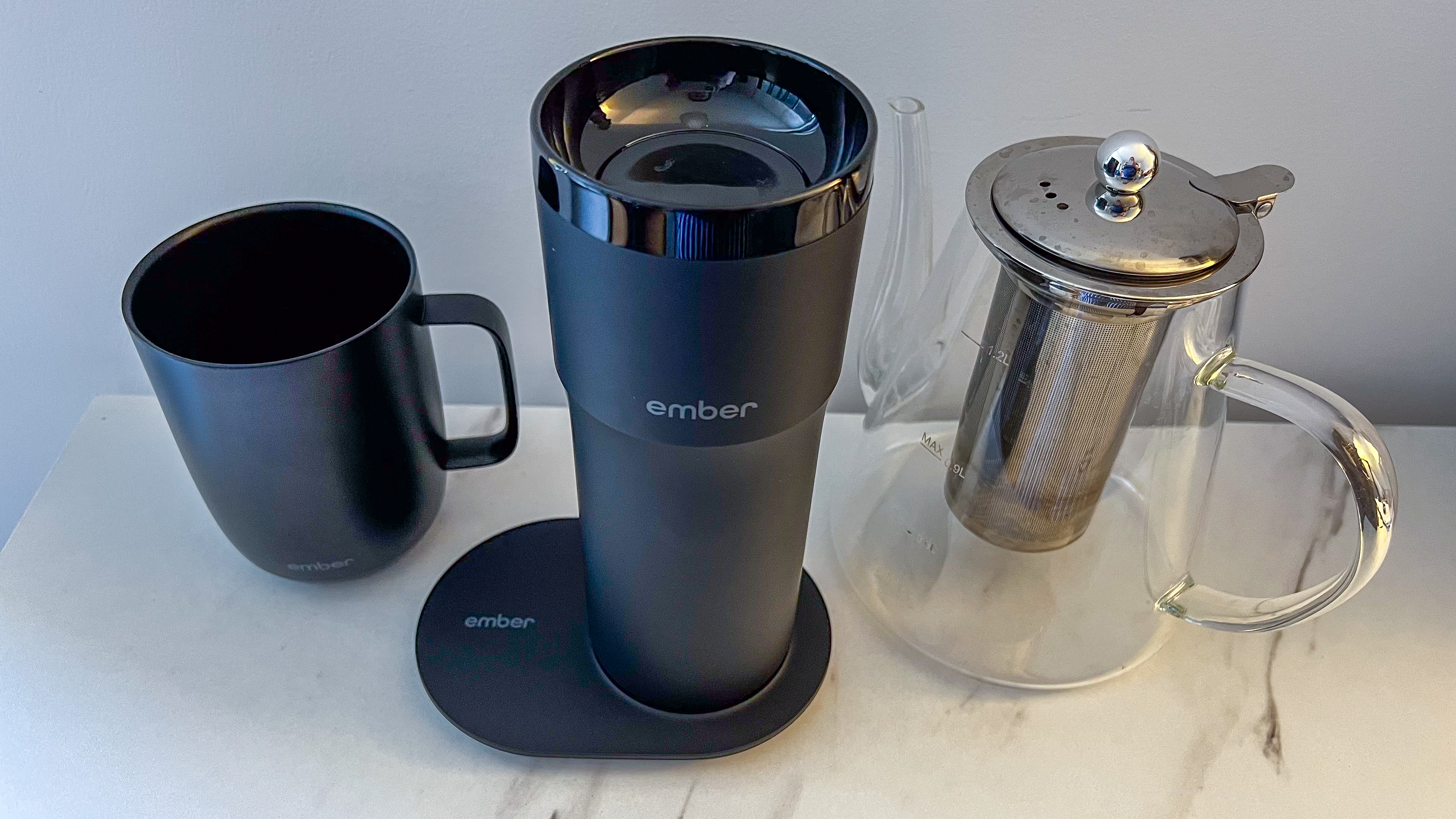 Ember Travel Mug 2+ on its charging plate sitting between the Ember Mug 2 and a glass kettle